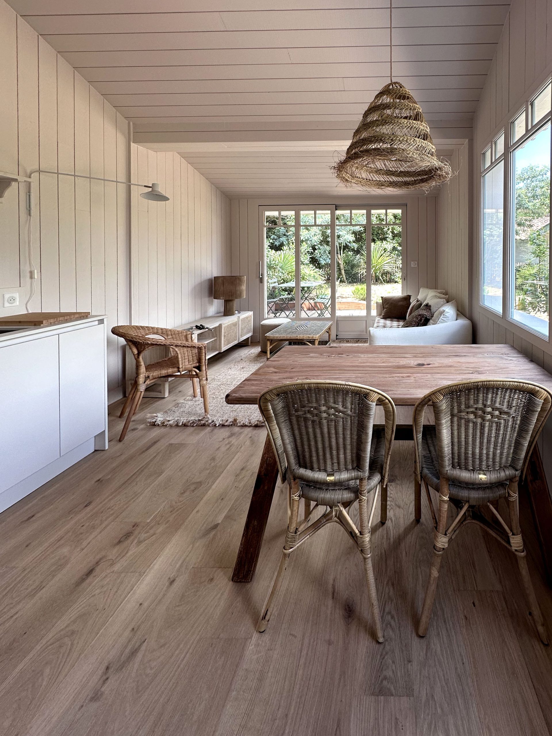 Tavolo in legno con sedie in vimini davanti a grandi finestre nella casa vacanze a Cap Ferret con cucina Zecchinon di Quartier Cuisine